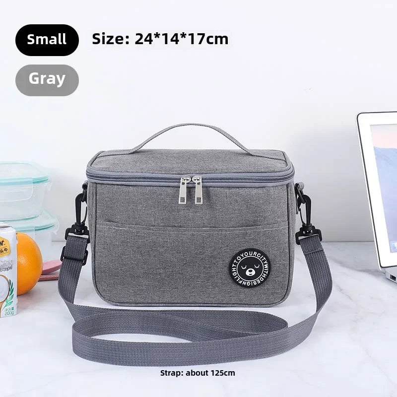 A gray insulated lunch bag with a strap is shown on a white marble surface.