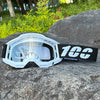 White motocross goggles with black strap resting on a gray rock outdoors.