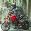 A person wearing a black helmet and dark clothing sits on a red Ducati motorcycle with a hip pack.