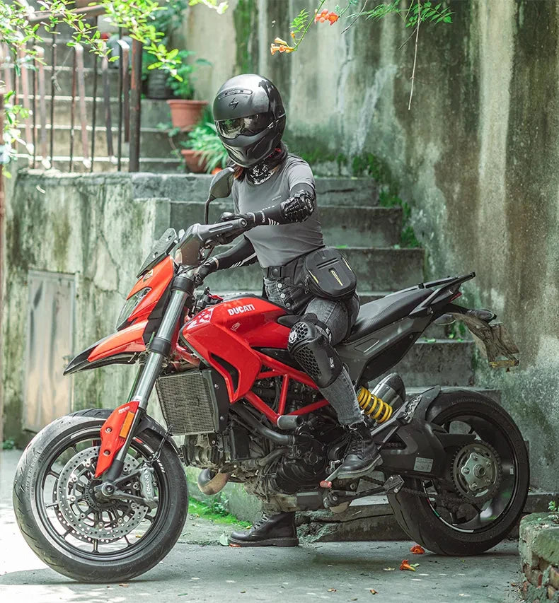 A person wearing a black helmet and dark clothing sits on a red Ducati motorcycle with a hip pack.