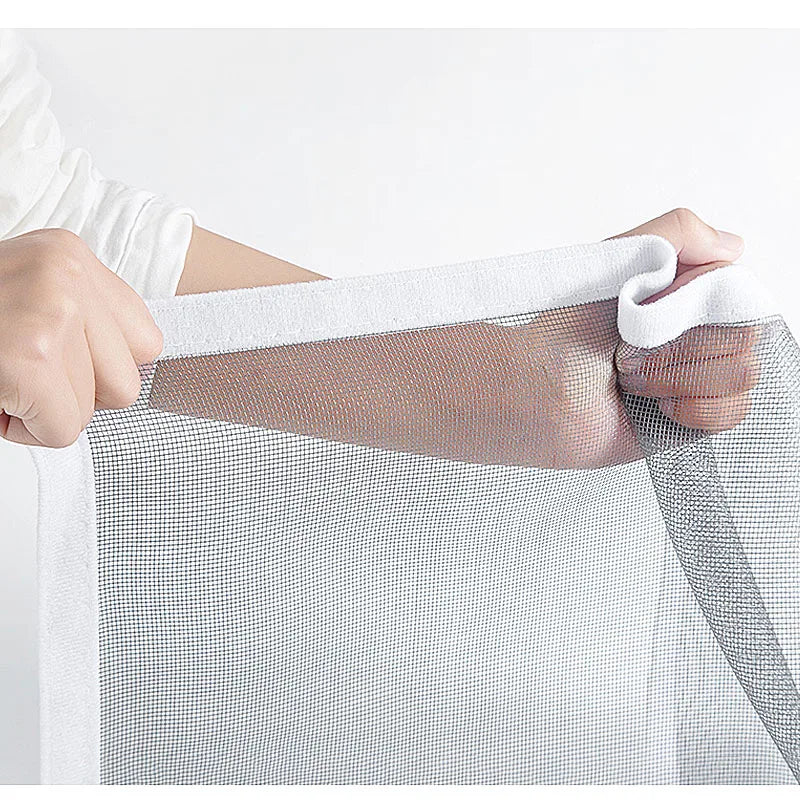 A hand is holding a clear self-adhesive window screen mesh with a zipper, showing the fine netting material.