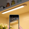 A hand holds a smartphone displaying a view of an interior cabinet light setup.
