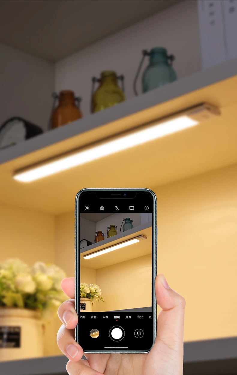 A hand holds a smartphone displaying a view of an interior cabinet light setup.