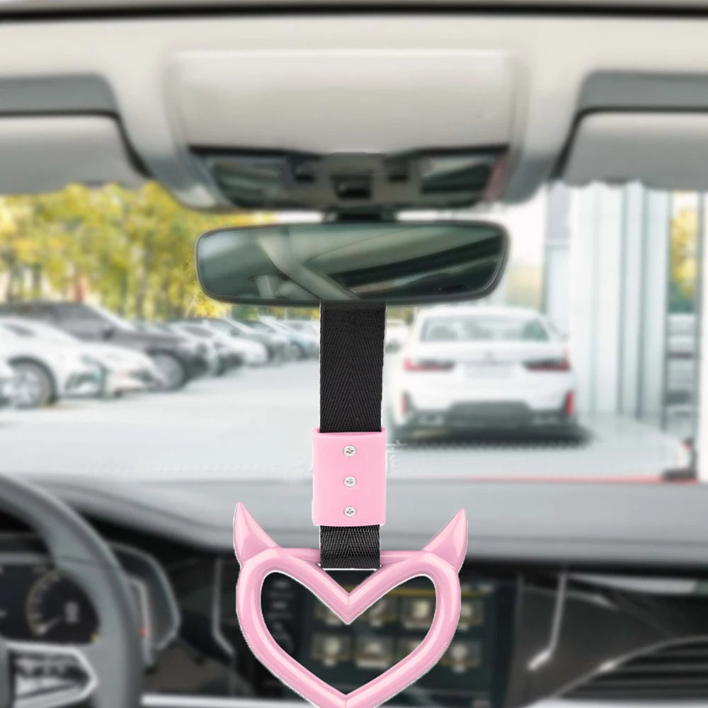 A pink heart-shaped ring drift handle with a strap is shown attached to a car rearview mirror.