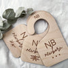 A set of seven wooden baby closet divider hangers with newborn and newborn labels resting on white fabric.