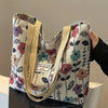 A beige corduroy tote bag with a floral pattern is held by a hand.
