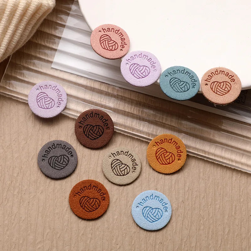 A collection of round, handmade PU leather labels in various shades of pink, purple, blue, and brown scattered on a light woo