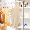A wooden baby closet divider set displaying several light-colored baby bodysuits on a white hanger.
