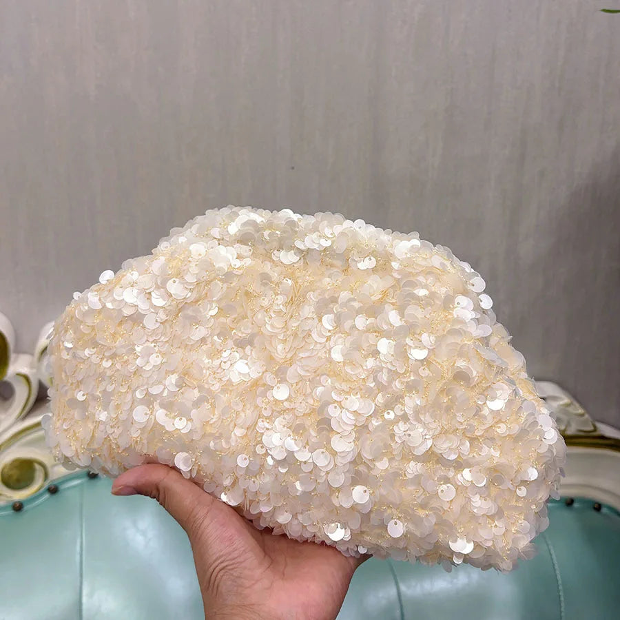 A hand holds a light beige sequin beaded chain shoulder clutch bag.