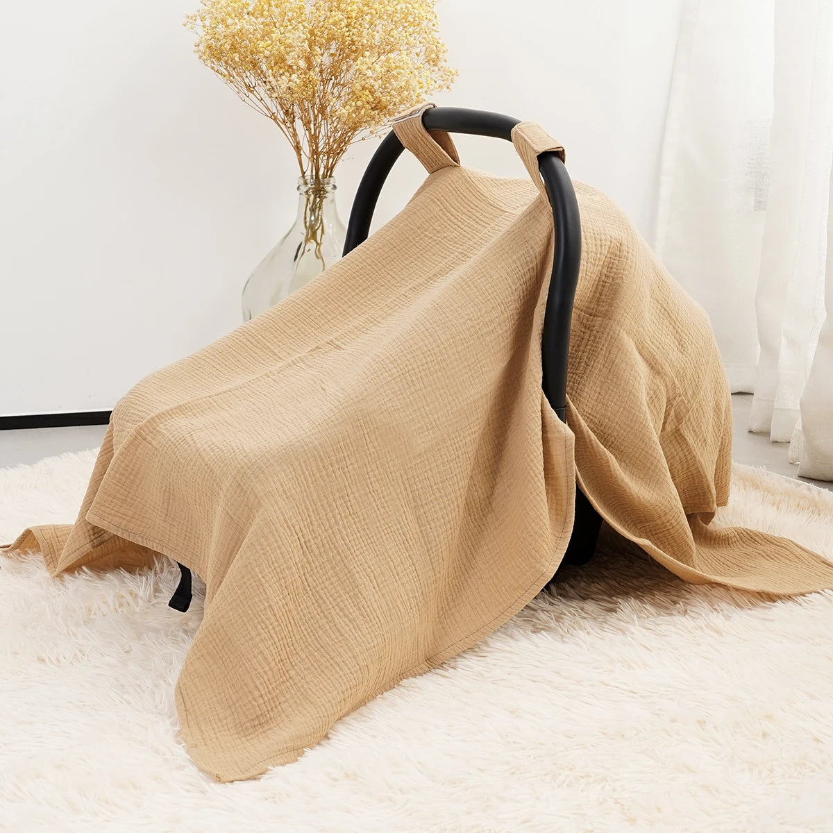 A beige breathable cotton muslin car seat and stroller cover draped over a black fabric frame on a white rug.