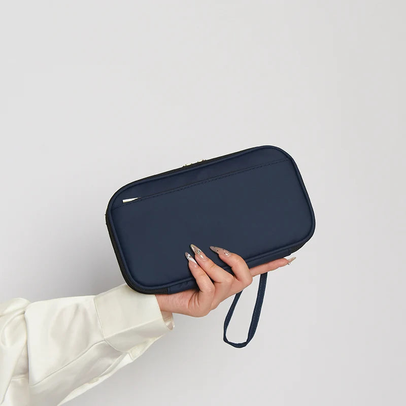 A hand holds a dark navy waterproof family passport and document organizer wallet.