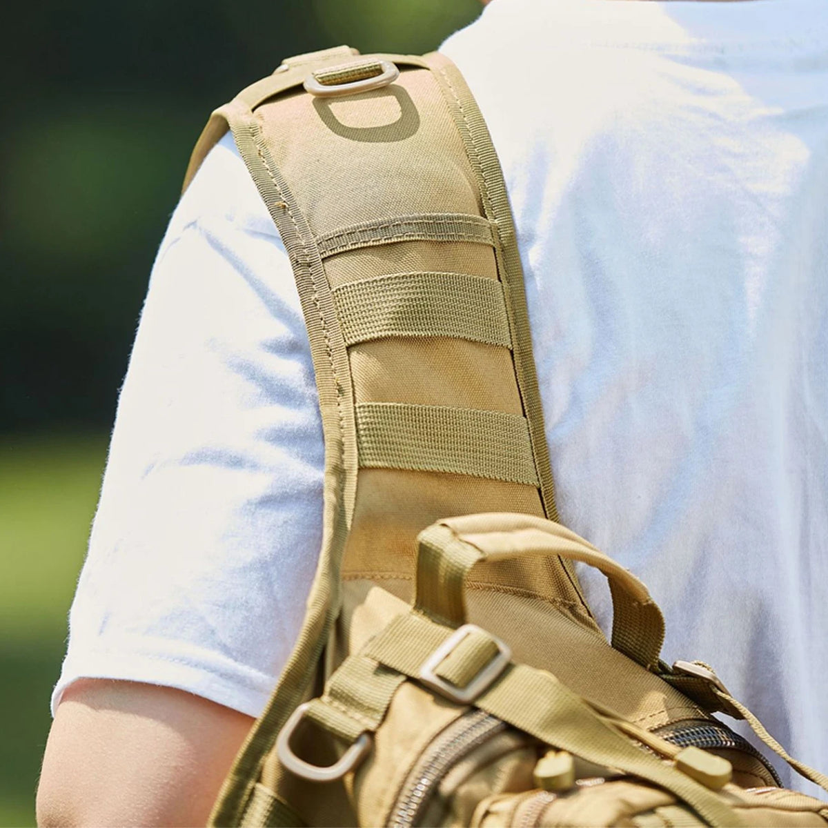 A close-up view of a tan crossbody chest bag with multiple zipper compartments and a MOLLE system worn on a person's torso.