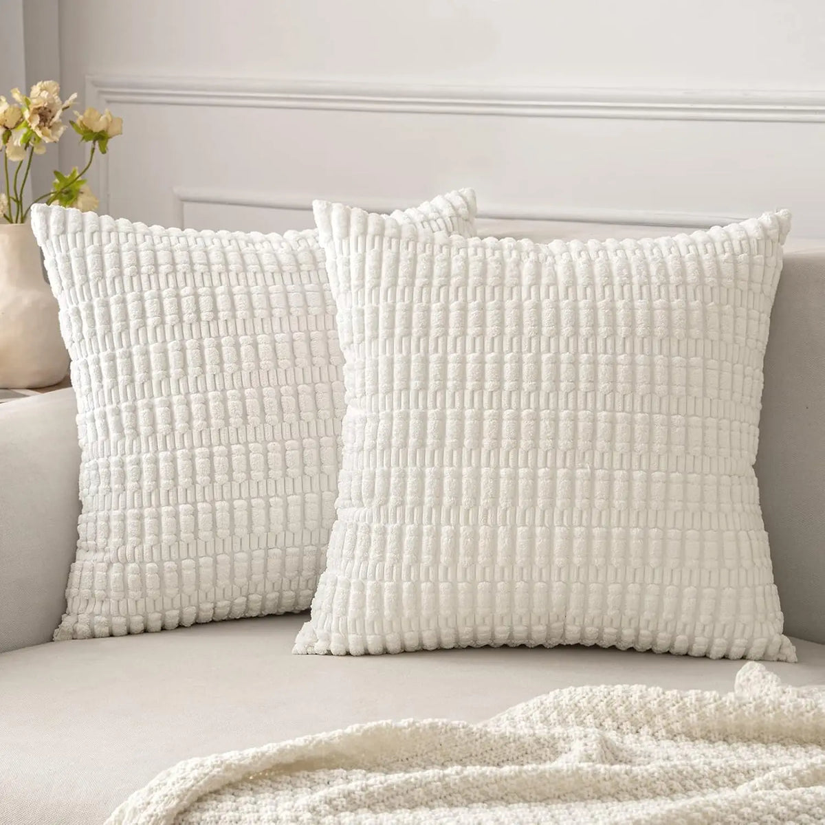 A white knitted textured throw pillow cover with a subtle vertical ribbed pattern on a light gray sofa.