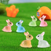 A set of six cute resin miniature bunny figurines in various pastel colors sitting on green grass.
