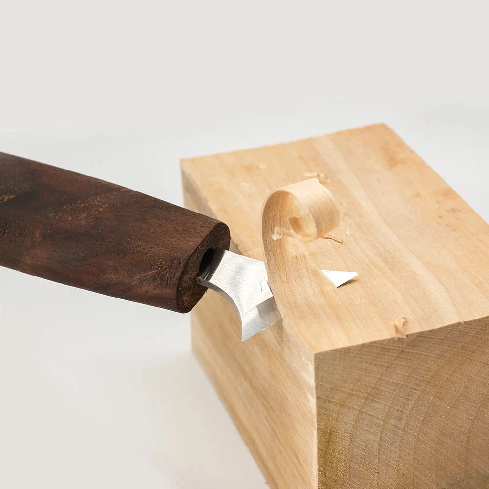 A close-up of a wood carving tool with a walnut handle being used to carve a piece of light-colored wood.