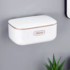 A white two-tier draining soap holder with a gold trim mounted on a gray wall.