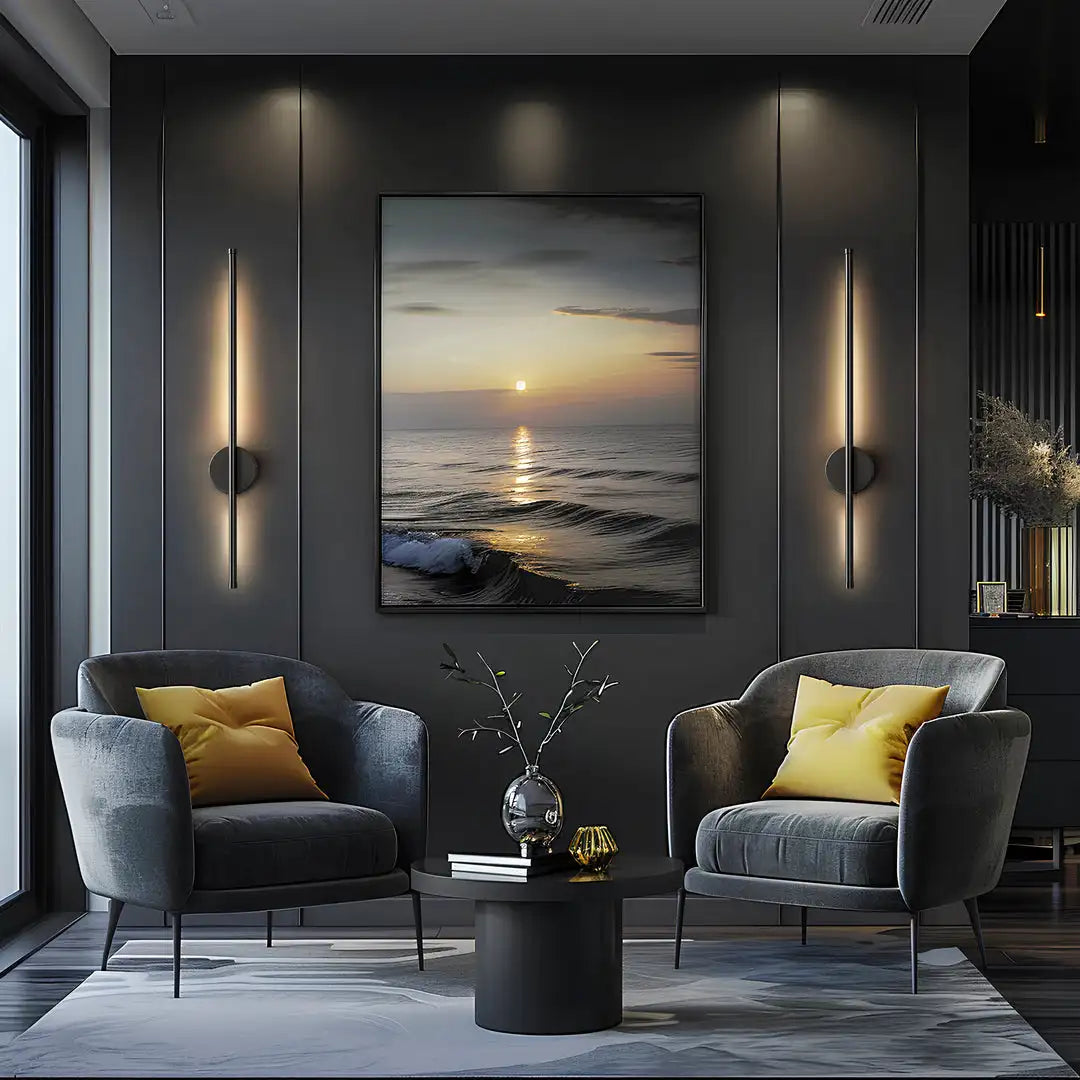 A modern living room featuring dark gray armchairs and wall sconces with warm light illuminating a large piece of art.