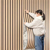 A person is touching a vertical wood grain wall panel, showcasing the texture and design of the self-adhesive wood panels.