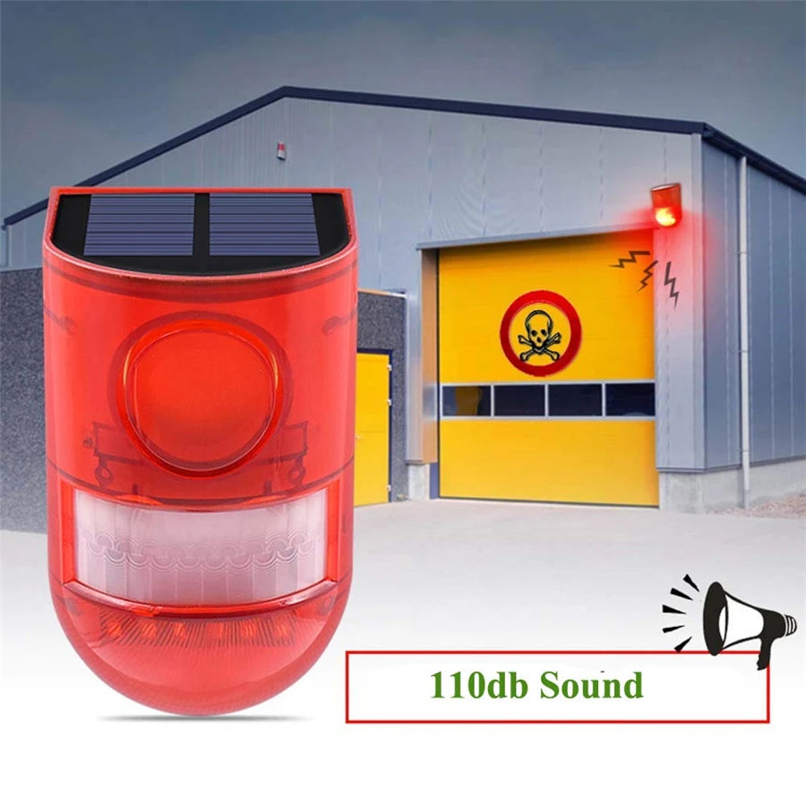 A red solar-powered motion sensor alarm with a strobe light is shown in an outdoor setting.