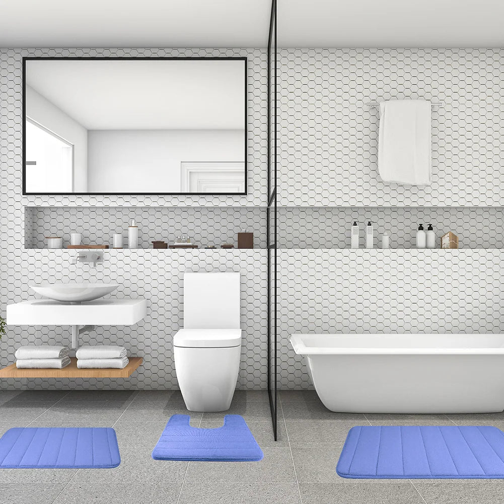 A modern bathroom featuring a toilet, sink area, and a white bathtub with blue bath mats on the floor.