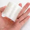 A hand holds a spool of clear elastic cord used for jewelry making or beading.