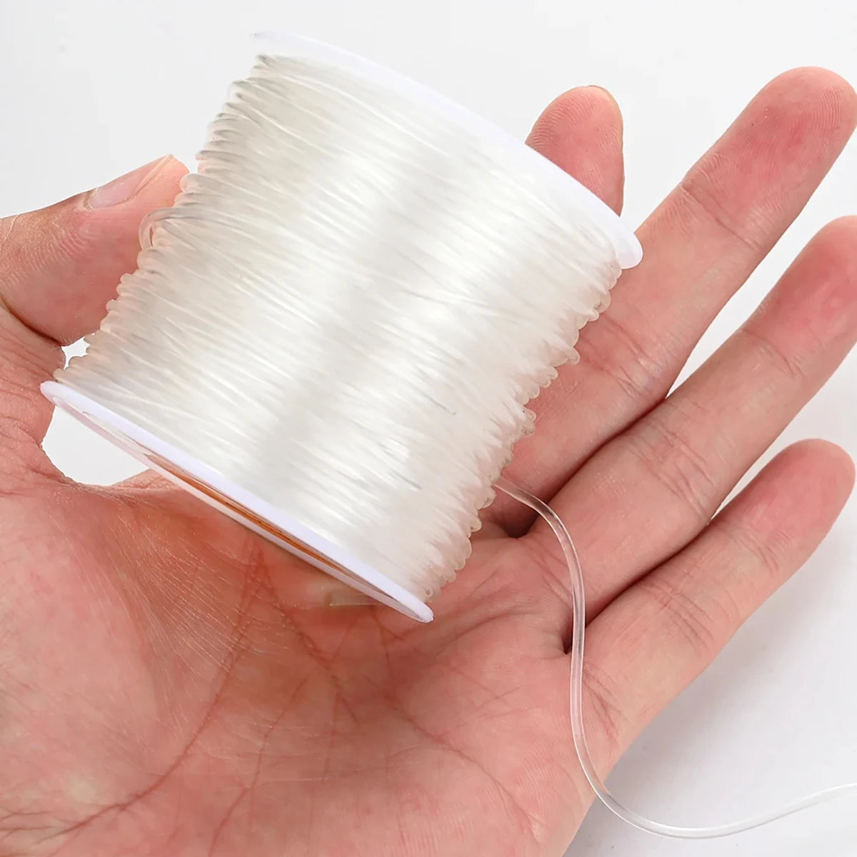 A hand holds a spool of clear elastic cord used for jewelry making or beading.