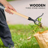 A hand holds a wooden three-stage handle weed puller with black jaws, used to pull weeds from the ground.