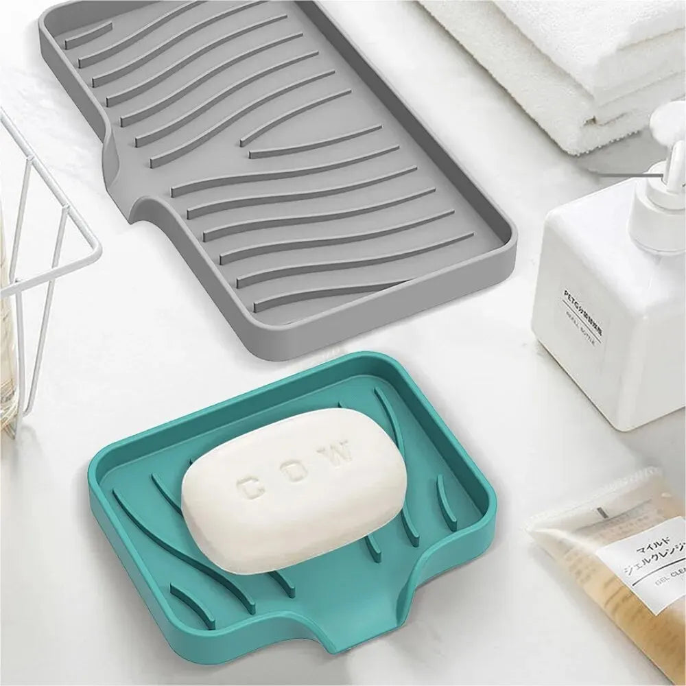 A teal silicone soap tray holding a white bar of cow soap, next to a gray silicone draining mat.