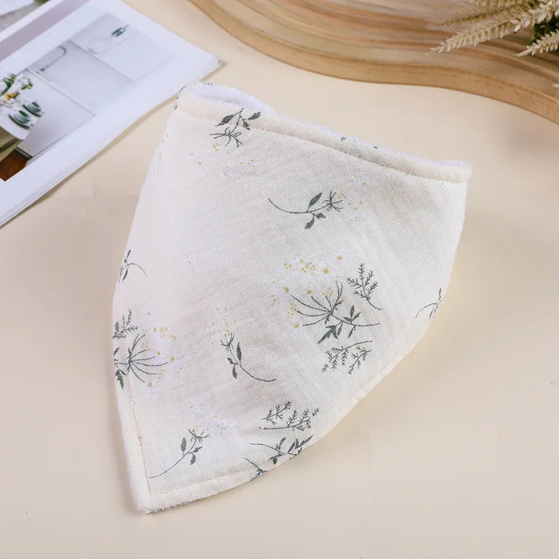 A white soft cotton baby bib with delicate gray and gold botanical embroidery, shown on a light background.