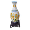 A white ceramic vase with yellow floral designs and blue accents, displayed on a dark stand.