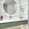 A bathroom vanity featuring white marble countertop and a large circular mirror surrounded by a green and white leaf pattern.