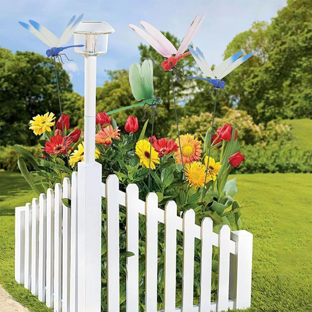White picket fence display featuring lifelike dragonfly garden clips with insect repellent designs and colorful flowers.