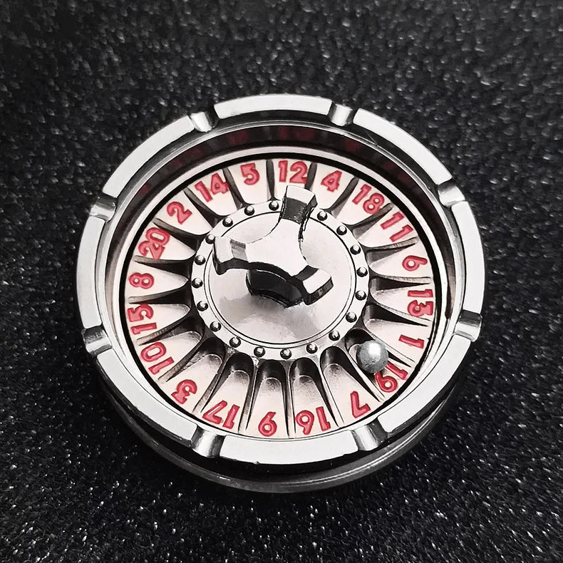 A close-up of a metal fingertip gyro roulette dice with numbered faces resting on a dark surface.