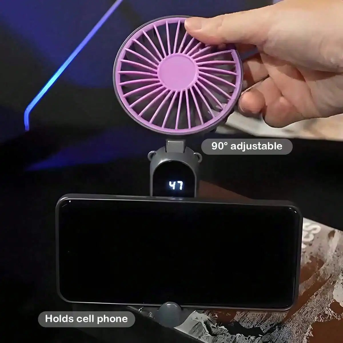Una mano ajusta un ventilador oscilante morado con ajuste de 90 grados sobre un smartphone negro.