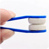 A hand holds a blue cleaning brush with two white microfiber pads for cleaning glasses.