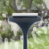 A dark cleaning brush with a white cleaning pad is shown against a background of water droplets and a green outdoor scene.