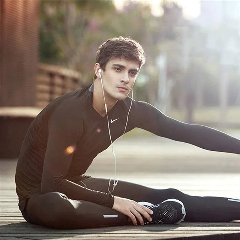 A young man wearing a black long-sleeved shirt is sitting outdoors, looking towards the camera.
