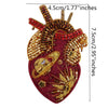 A detailed image of a large, heart-shaped patch made of red fabric and gold and red beads and rhinestones.
