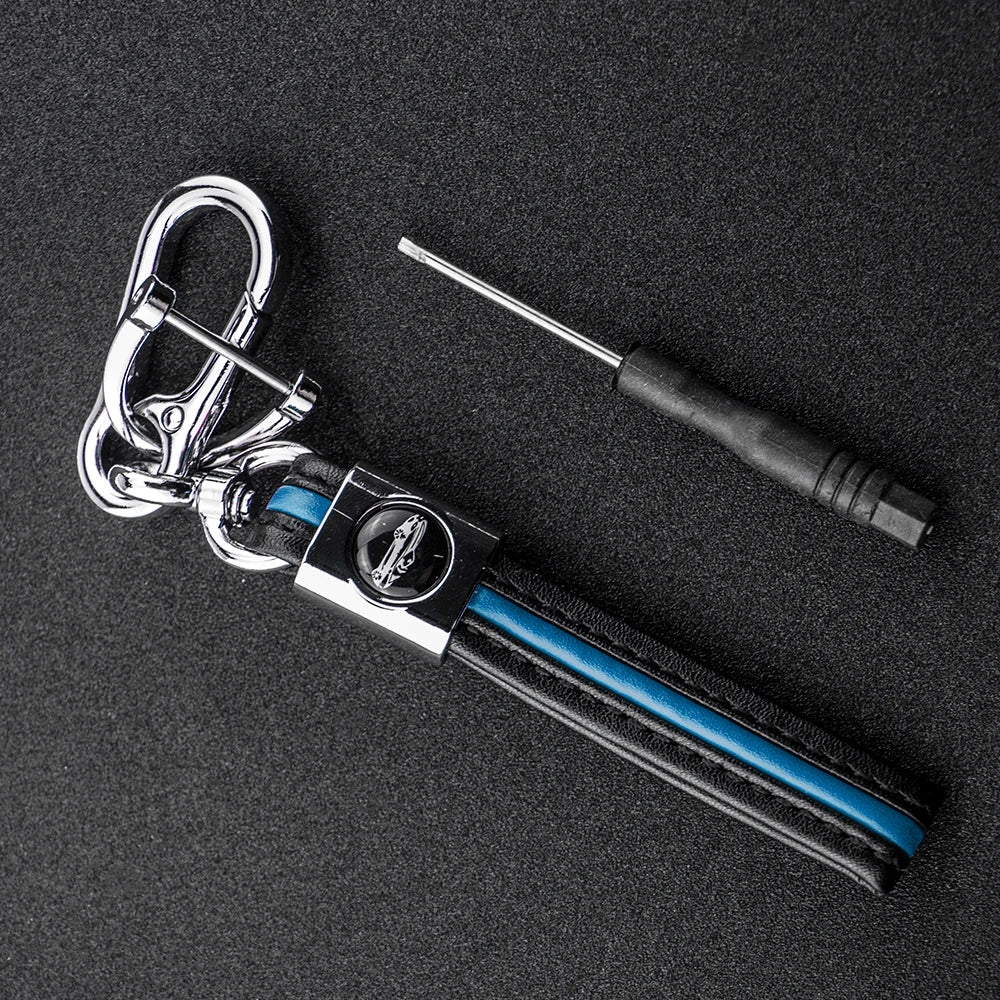 A silver key fob with a black protective TPU cover and a metal tool is displayed on a dark surface.