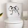 A white toilet lid features a black sticker depicting an expressive, angry face.