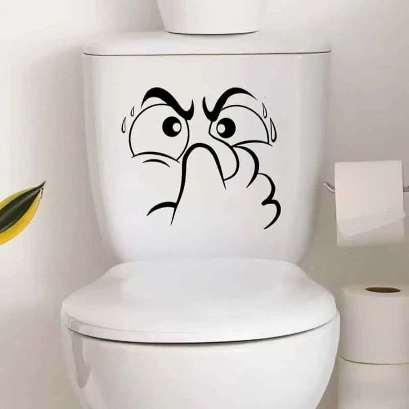 A white toilet lid features a black sticker depicting an expressive, angry face.
