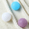 Three reusable laundry balls in light blue, white, and purple resting on a white textured fabric.