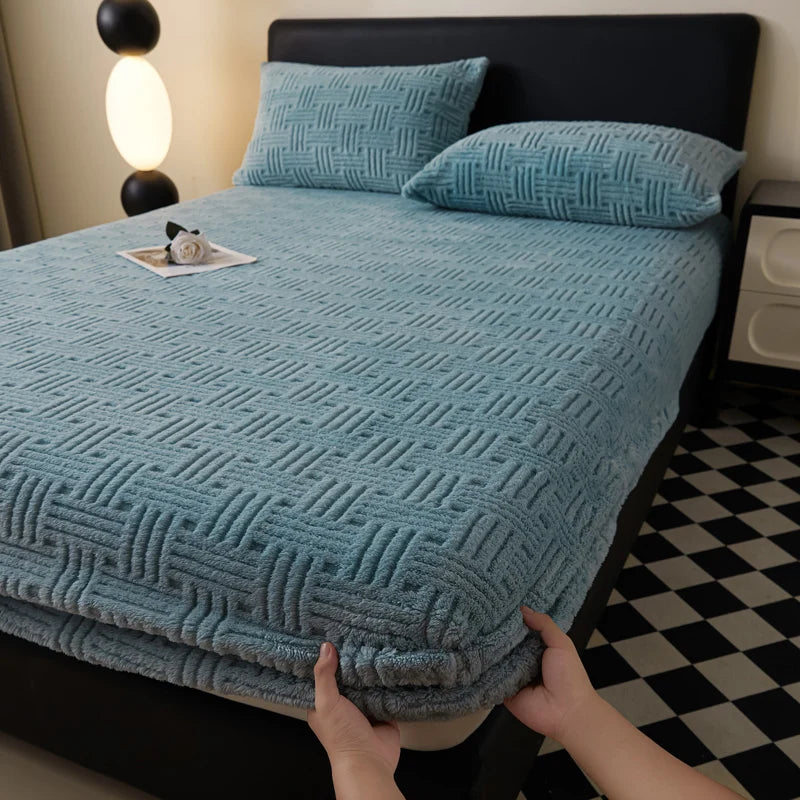 A teal plush mattress cover with an elastic edge is shown on a bed, with hands adjusting the fabric.