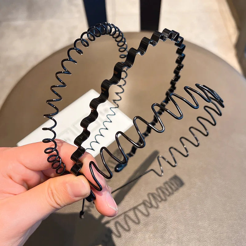 Eine Hand hält mehrere schwarze, elastische Kopfband mit variierenden Spiralformen vor einem neutralen Hintergrund.