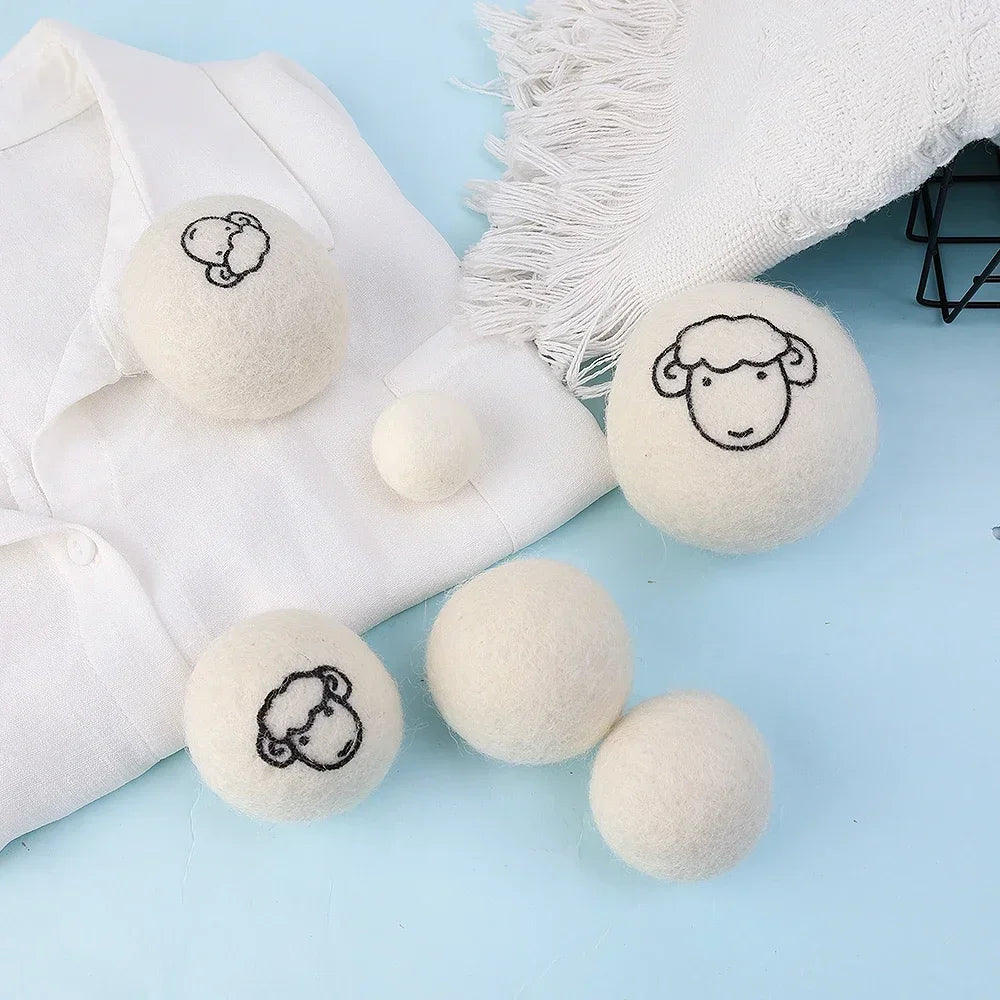 A set of six natural wool dryer balls in various sizes resting on a white fabric background.