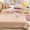 A pink cartoon pattern kids lightweight summer quilt displayed on a bed with white curtains and a stuffed animal.