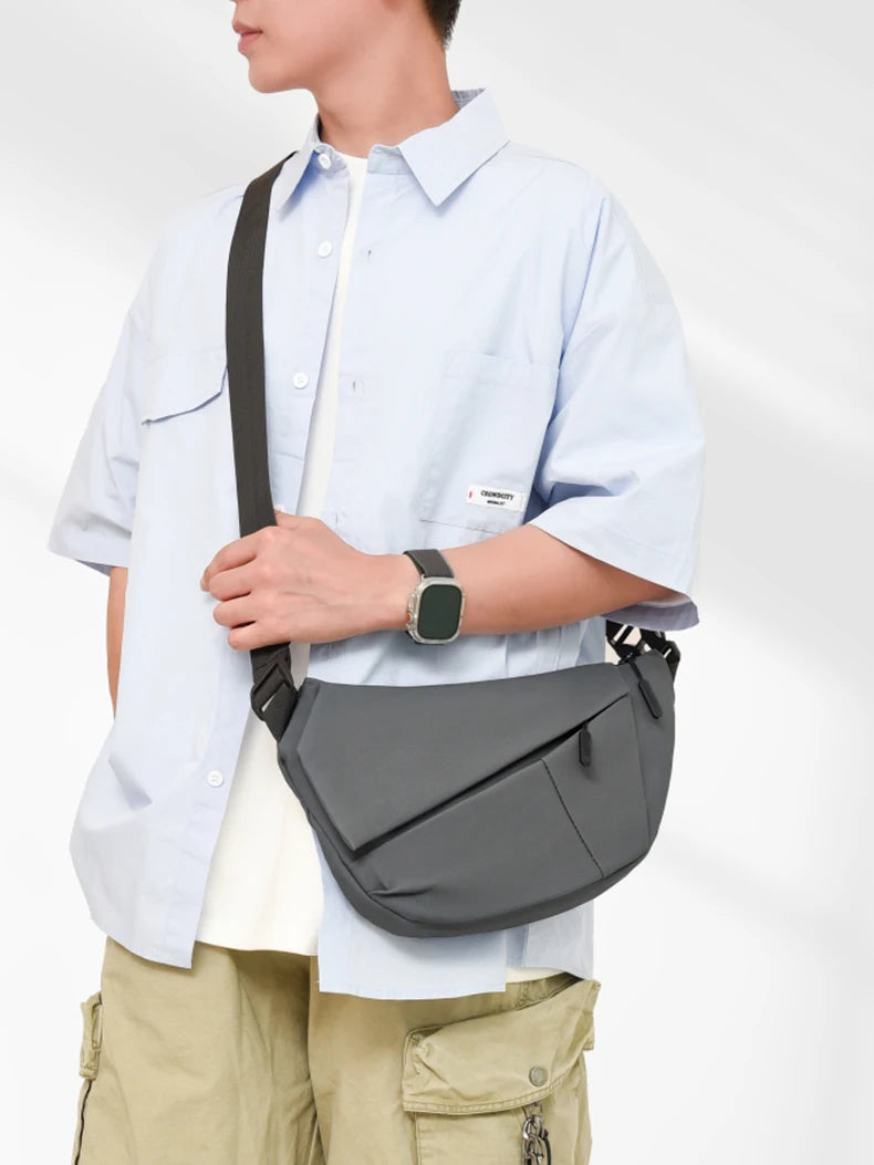 A man wearing a light blue shirt and khaki pants carrying a gray practical chest bag across his body.