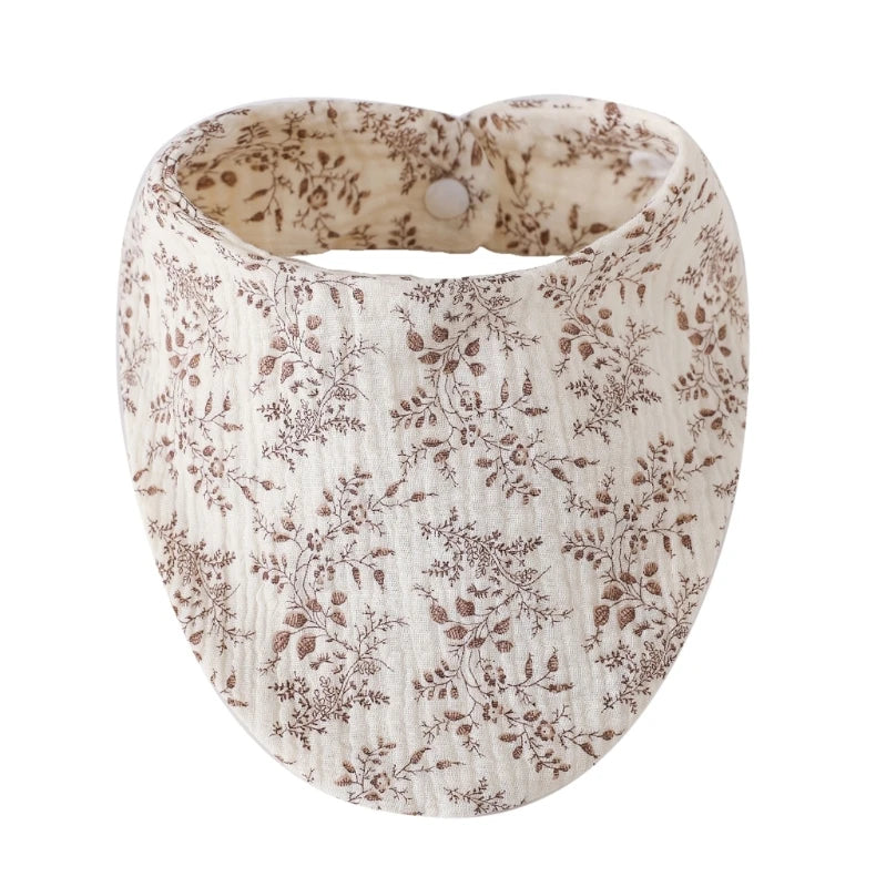 A beige organic cotton muslin baby bib with a floral print and an absorbent band.