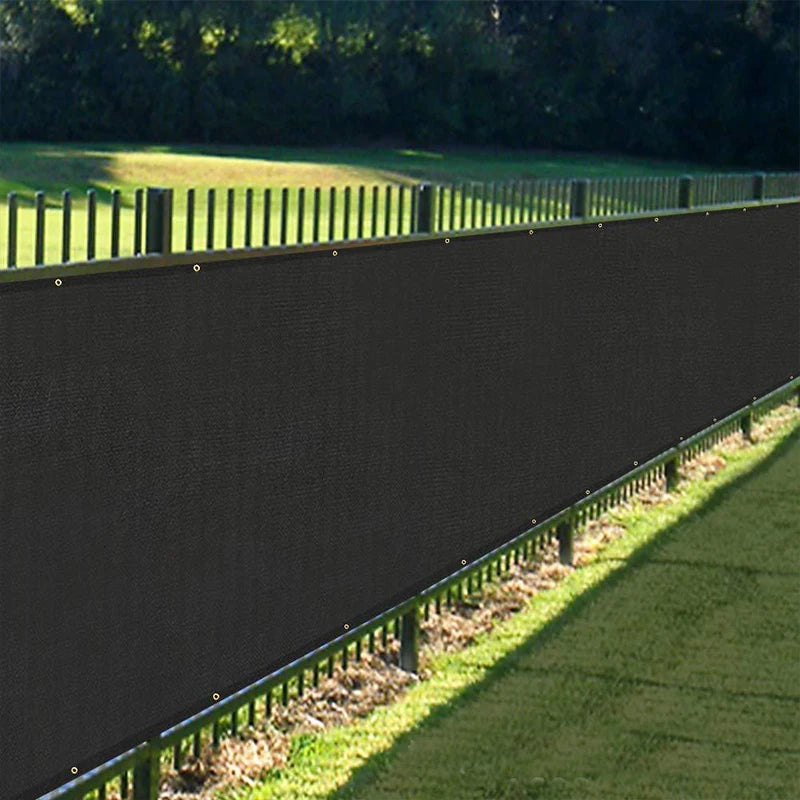 A dark gray HDPE privacy screen installed along a fence line in a grassy outdoor area.