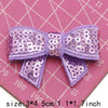Purple sequin bow patches for DIY crafts displayed on a pink grid background.